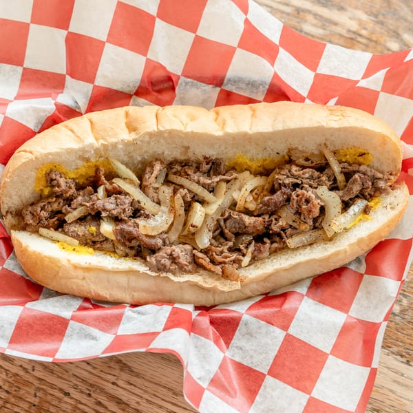 Cheesesteak sandwich with steak, onions, and mustard on a hoagie roll, wrapped in red and white checkered paper.