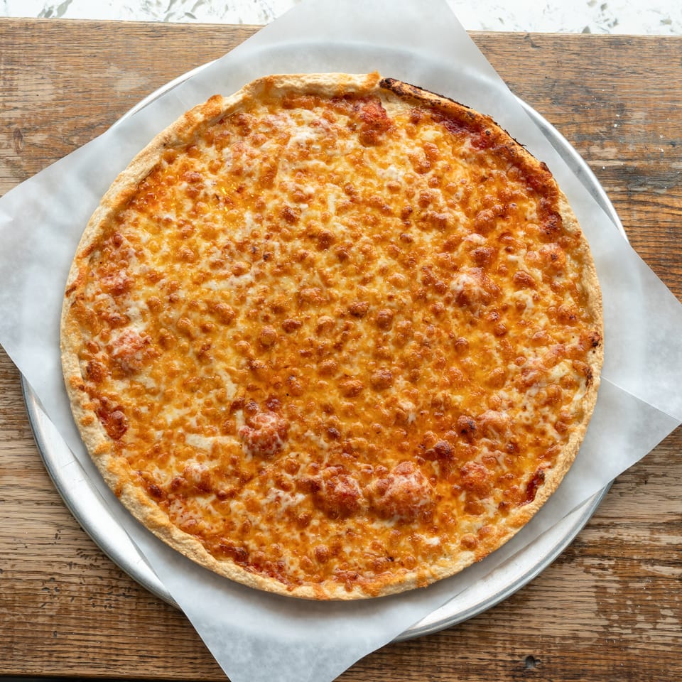 A whole cheese pizza on a metal tray with parchment paper, on a rustic wooden table.