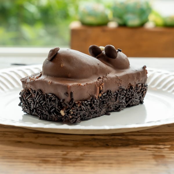 A chocolate cake shaped like a mouse, covered in sprinkles, on a white plate.