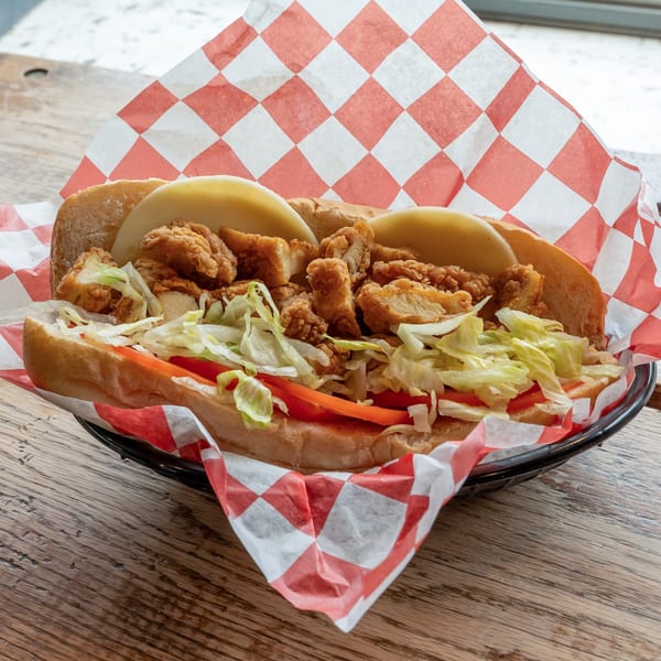Fried chicken po'boy sandwich with lettuce, tomato, and cheese on a wooden table.