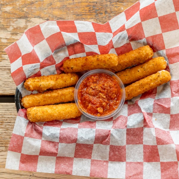 Golden-brown mozzarella sticks with a side of marinara sauce in a red and white checkered basket.
