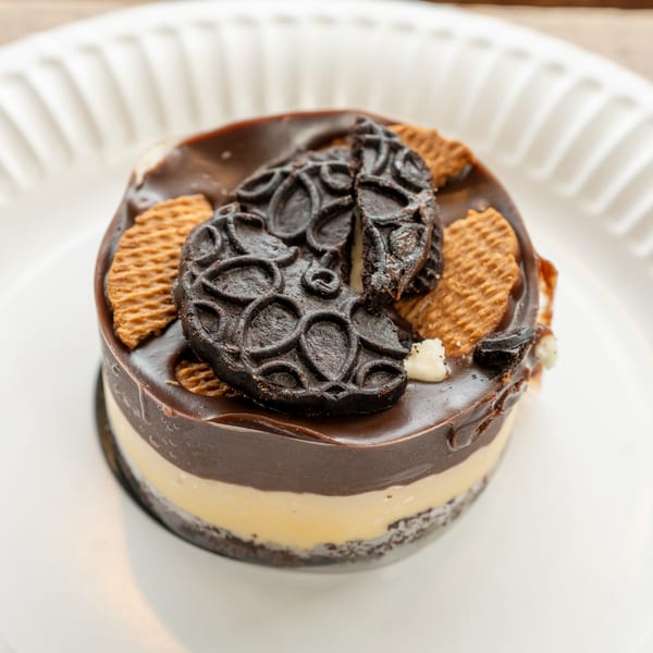 A layered dessert with chocolate and cream, topped with cookies, on a white plate.