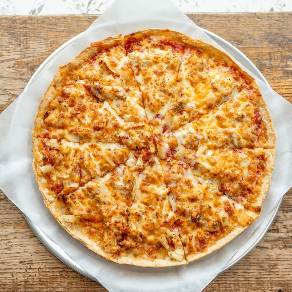 A whole, sliced chicken and pineapple pizza with melted cheese on a metal tray.