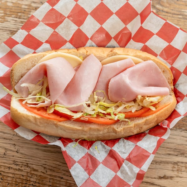 Ham and cheese sub sandwich with lettuce and tomato on a red and white checkered paper.