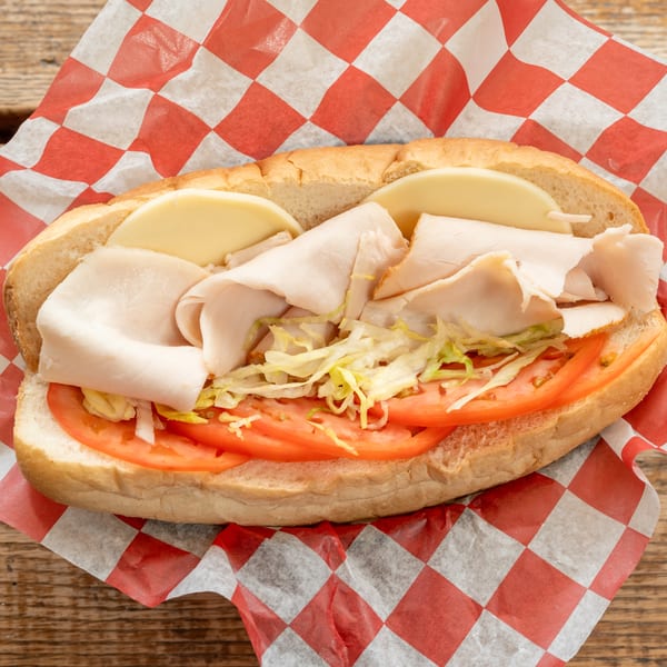 Turkey and cheese sub sandwich with lettuce and tomato on a red and white checkered wrapper.